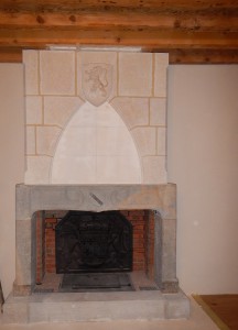 Habillage de la hotte de cheminée en pierre bouchardée, taille d'un arc en ogive. La clé de l'arc est orné d' un blason sculpté du lion de Franche-Comté.